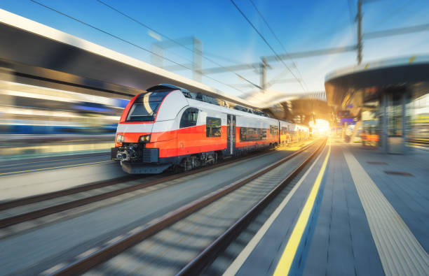 istock High-speed orange passenger train moving at railway station platform at sunset. Train station. Modern railway transportation concept with blurred motion effect. Railroad. Commercial transport 2158316474
