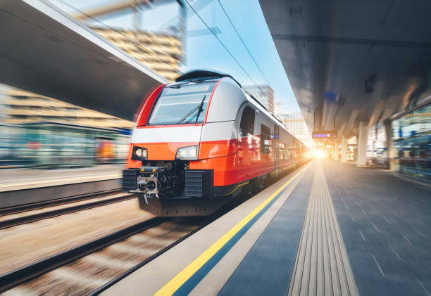 istock High-speed orange passenger train moving at railway station platform at sunset. Train station. Modern railway transportation concept with blurred motion effect. Railroad. Commercial transport 2158316487