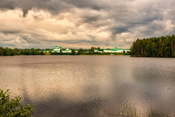 Russia, Leningrad region, Holy Trinity\nAlexander Svirsky Monastery, 08/09/2023. on the shore of Lake Roshchinskoye. evening, a light breeze ripples the water. Dense cumulus clouds cover the sky, allowing sunlight to shine through.