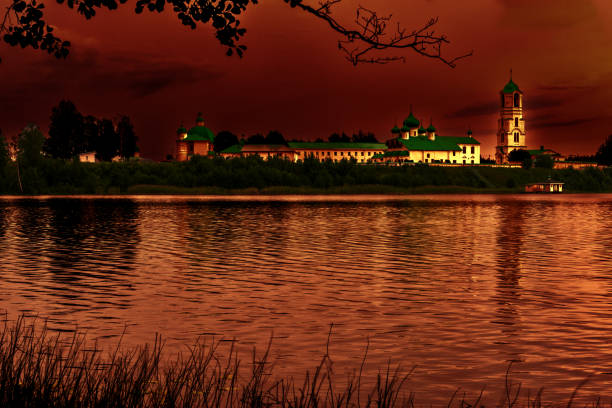 Russia, Leningrad region, Holy Trinity\nAlexander Svirsky Monastery, 08/09/2023. on the shore of Lake Roshchinskoye. Late evening, twilight, a light breeze rippling the water. Everything is painted in dark orange colors by the setting sun.