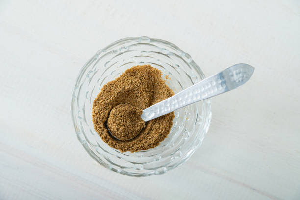 Cumin on mini glass bowl with rustic metal spoon on the inside, taking a portion of the spice