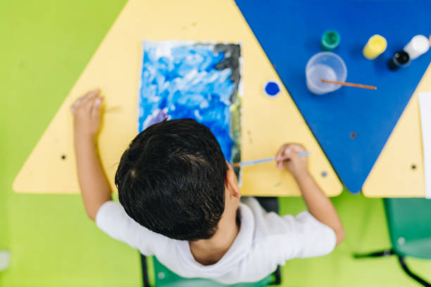 Boy drawing and painting with paintbrush at school classroom