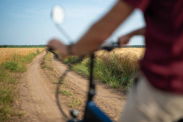 Mature man on bikepacking solo trip with electric bike, passing in golden wheat fields with wind turbines. Sustainable lifestyle.
