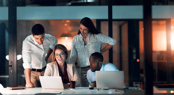istock Collaboration, team diversity and office at night for deadline, strategy and explanation with laptop. Female leader, group and workshop for learning, growth and development in workplace in evening 2158336293
