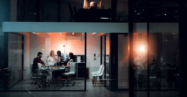 Discussion, night and teamwork with laptop in boardroom, banner and deadline for project and planning. Collaboration, online and business people, proposal and talking for financial records in dark