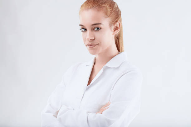 Confident scientist in lab coat smiling, arms crossed, exuding expertise in healthcare and science against white background. Young adult redhead showcases successful career in medical research