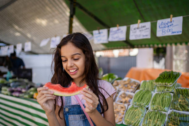 istock Girl eating fresh fruit outdoors in the public fair 2158341846