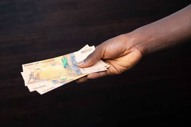istock Black hand holding Ugandan shilling notes over dark background, currency of Uganda 2158343099