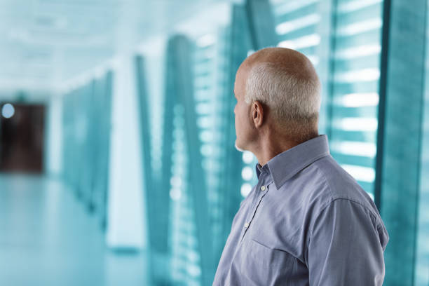 Senior businessman is standing in a modern office building, looking out the window at the city. He is deep in thought, contemplating the challenges and opportunities that lie ahead