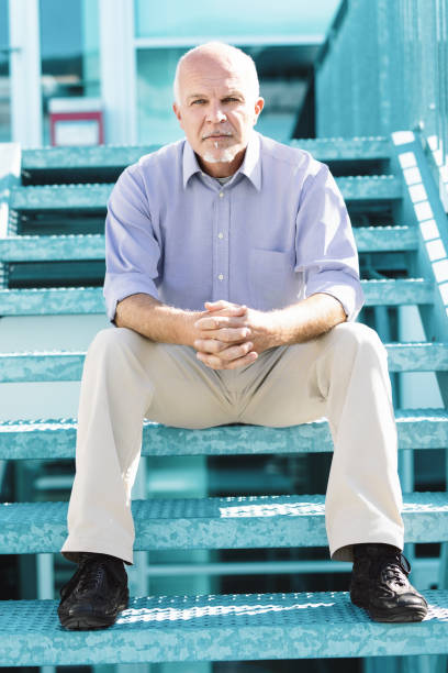 istock Bald man sitting, hands clasped, bright stairs 2158346953