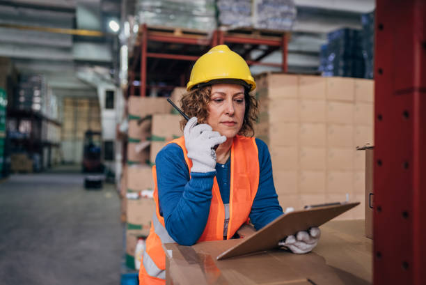 istock Focused and in control, a female warehouse manager coordinates operations via walkie-talkie amidst the bustling aisles of inventory 2158348521
