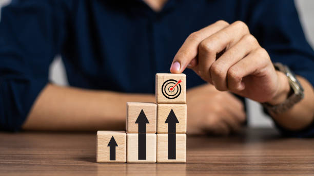 istock businessman hand pointing on dart board and arrow icon go up on wooden cube block stack, target plan, company growth, market trend, finance, strategy, business start up concept 2158352162