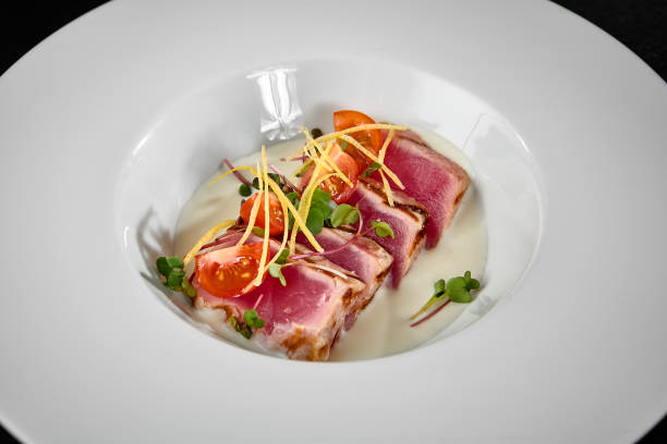 Elegant Tuna Tataki Dish Garnished with Microgreens and Cherry Tomatoes on White Plate.
