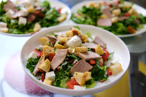 Close-up of Caesar Salad. Plate with Culinary Masterpiece. Spoon Chef Adds Thick White Sauce. Mayonnaise. Seasoning. Savory Salad Dressing. Tomatoes. Fried Chicken Breast. Caesar salad dressing