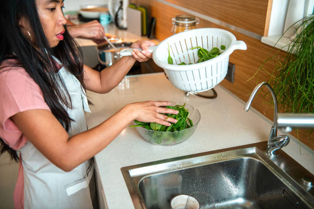 A Hispanic man and an Asian woman prepare a meal together, showcasing teamwork in a bright kitchen, wearing casual clothing and using kitchen utensils.