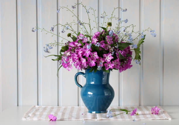 primroses and forget-me-nots in a jug on the table in a white wooden cottage. springtime, rural composition. flowers in a vase.
