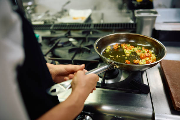 Close up of chef preparing food in frying pan in the kitchen.