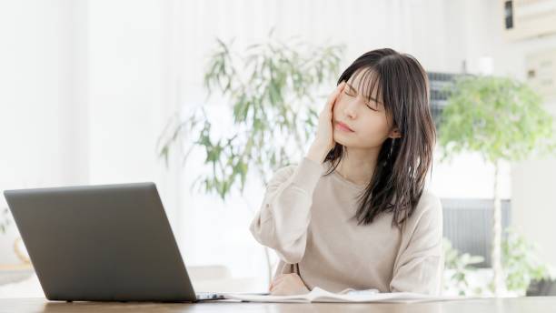 パソコンで作業中に頭痛を感じる女性 - 仕事 つらい 日本人 ストックフォトと画像