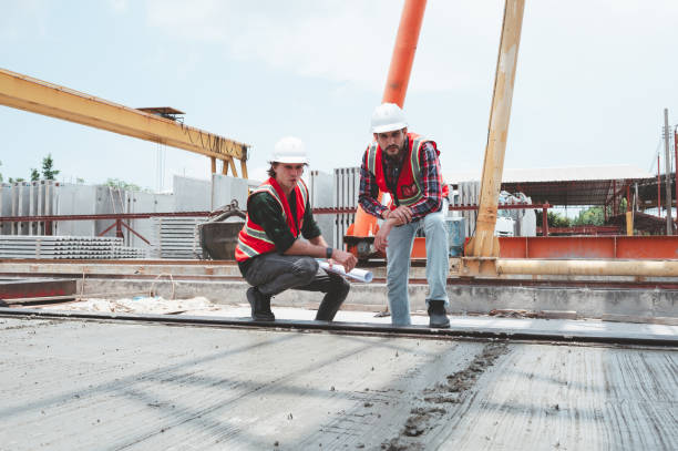 istock Engineer or architect with a hardhat examines the schedule on a set of plans. Two businessmen, both engineers, at the construction site. 2158374245