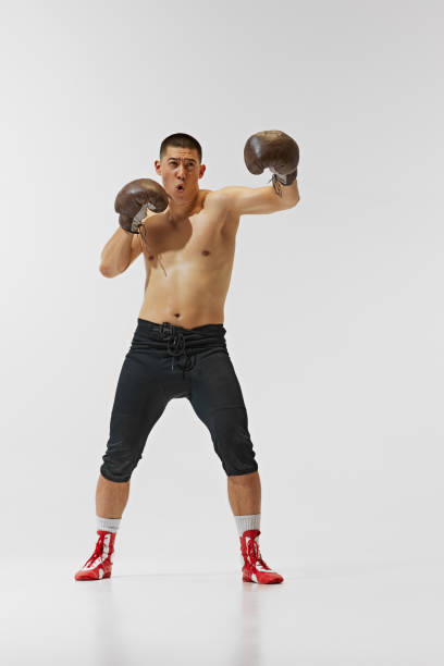 istock Shirtless emotional young man, young boxer training hard, captured mid-punch pose isolated on white background. 2158375055