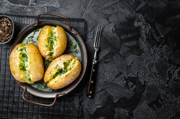 istock Baked Jacket potatoes with cheese, herbs and butter. Black background. Top view. Copy space 2158376325