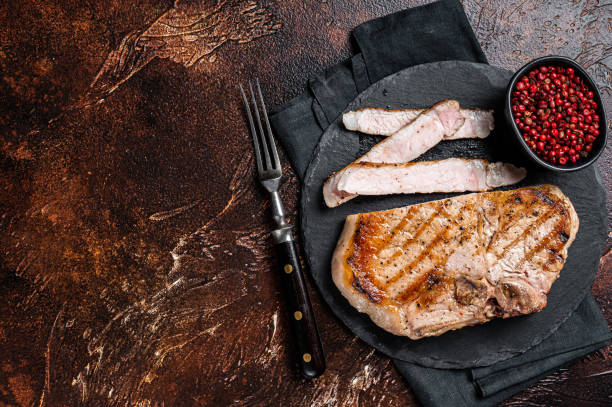 istock Roast BBQ pork Chop or T-bone meat steak sliced on a board. Dark background. Top view. Copy space 2158376389