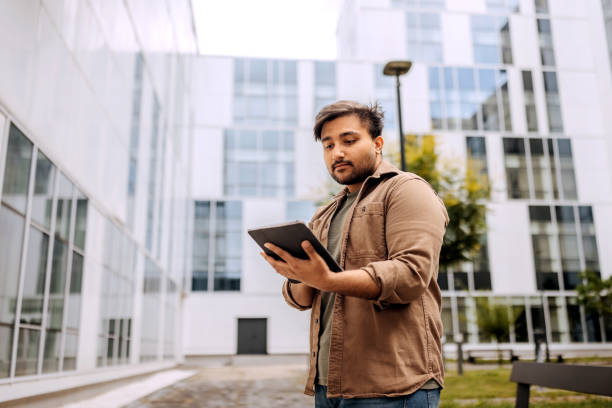 istock Young casually clothed man using digital tablet while standing in front of modern building in city 2158383962