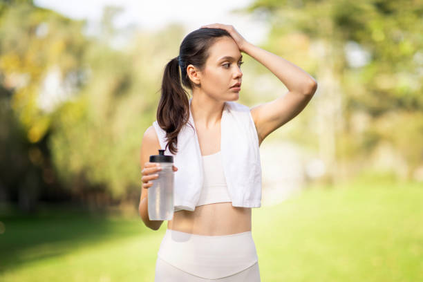 istock An attentive young woman wipes sweat from her forehead while holding a water bottle 2158385770
