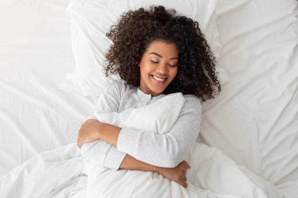 istock Smiling Young Woman Embracing White Pillow in Bright Bedroom Setting 2158385943