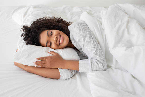 istock Woman Laying in Bed With Pillow, Smiling at Camera 2158385973
