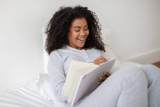 istock Young Woman Smiling While Relaxing, Writing in Notebook in Bed 2158386013