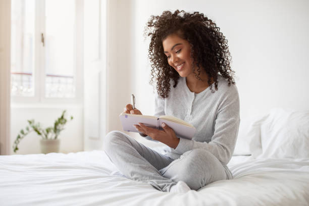 istock Woman Sitting on Bed Writing in Notebook 2158386146