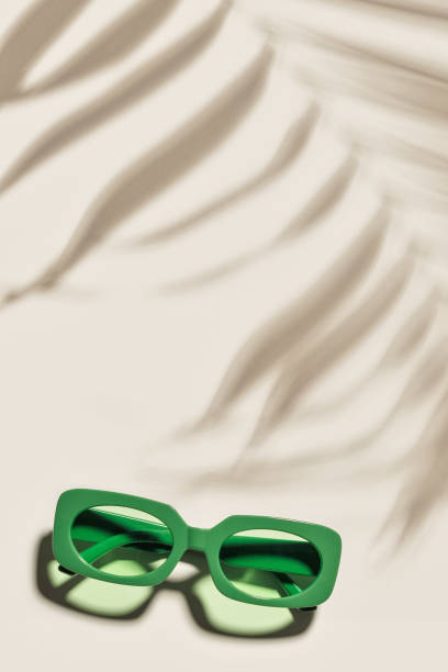 istock Green Sunglasses on beige colored background at sunlight with palm leaf shadow, summer plastic-framed glasses. Aesthetic top view eyeglasses, fashion eyewear, minimal trend, copy space, pastel 2158386271