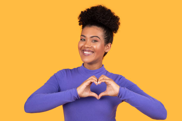 istock Woman Making Heart Gesture With Hands On Yellow 2158386342