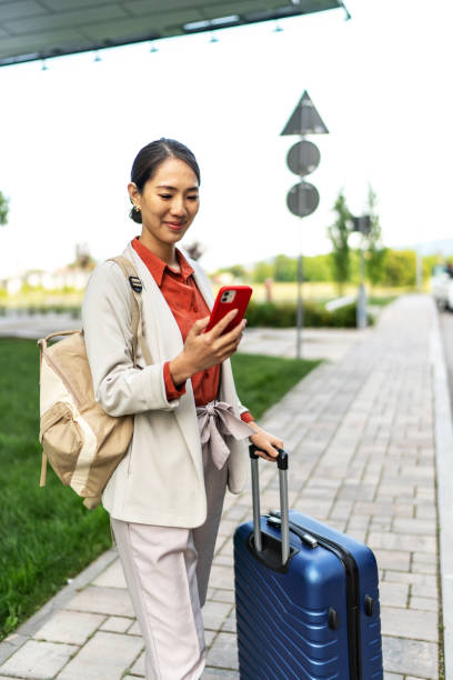 istock Asian woman using smartphone while carrying luggage 2158391168
