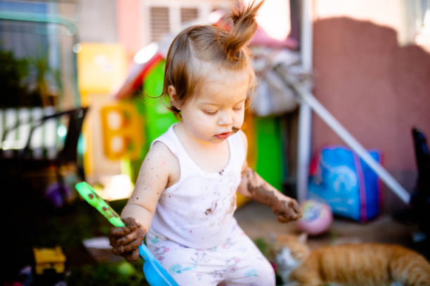 The little girl is playing in the yard with the plastic shovel and mud.