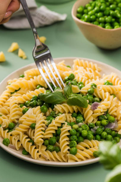 Woman eats vegan pasta with green peas and from plate closeup. Lady tastes fresh healthy dish with fusilli and vegetables at restaurant. Simple cuisine