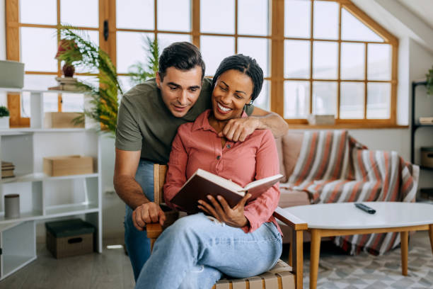 istock Smiling woman reading book while her husband is hugging her from behind 2158408414