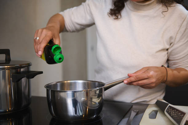 istock Woman pouring oil into pot while cooking in kitchen 2158409846