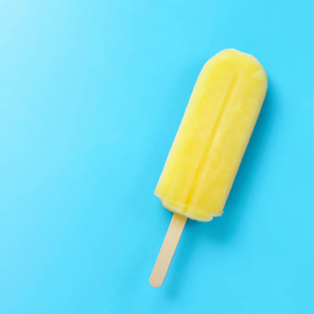 Close up of a yellow popsicle on the light blue background.