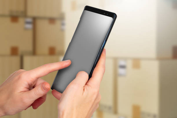 istock Phone mock up. Empty phone in hands of man. Smartphone with screen off. Cardboard boxes behind cellphone. Selective focusing. Place for your recommendation. Template for delivery application or site 2158414155