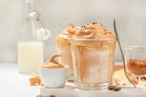Dalgona cream coffee whipping on cold milk In a transparent glass on light background