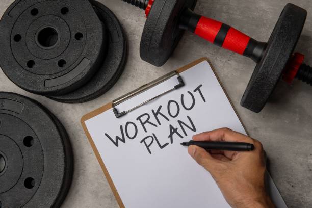 istock A close-up image of a clipboard with a WORKOUT PLAN written on it next to a black dumbbell and weight plates. 2158419272