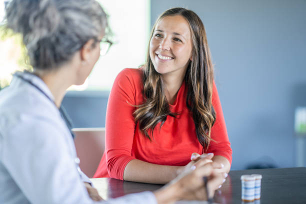 Women's Health Appointment A young woman sits with her female doctor in her office as they discuss her health concerns. The patient is dressed casually and has a smile on her face. red medical scrubs stock pictures, royalty-free photos & images