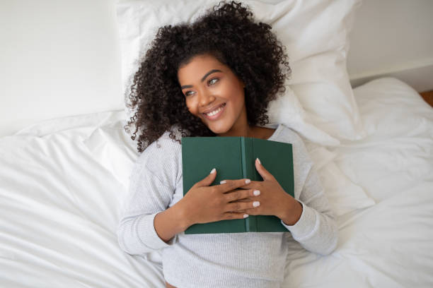 istock Woman Laying in Bed Holding a Book, Looking Away 2158420594