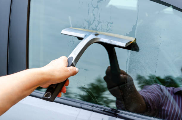 istock hand with squeegee brush washing car window. Manual car window cleaning with scraper. 2158421910