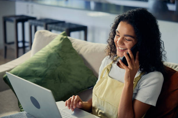 istock a woman is sitting on a couch using a laptop and talking on a cell phone 2158424635