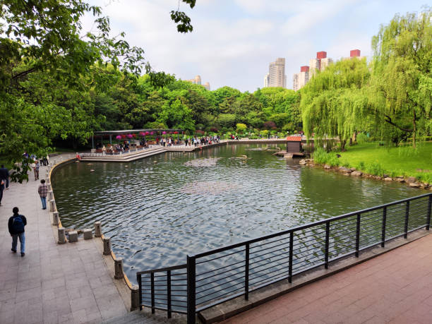People walking at the artificial lake in Xujiahui Park, a park in Xuhui District, Shanghai. It was built in 1999, on the former grounds of the Great Chinese Rubber Works Factory and the EMI Recording Studio.