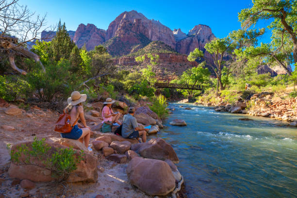 Family relaxing by the river on hiking trip in Utah Family sitting by the Virgin River . Pa'rus Trail. Zion National Park, Springdale , Utah, USA. zion river stock pictures, royalty-free photos & images
