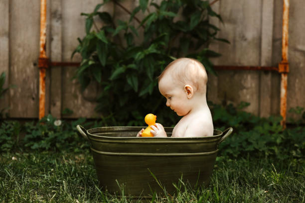 A one~year~old baby boy smiles at a rubber ducky as he sits in an antique tub in a garden. Shot with a Canon 5D Mark IV.